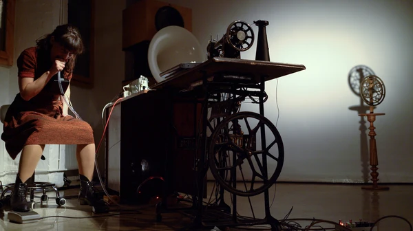 Picture of the performance by Lottie Sebes. It cointains the artists playing the Veritas Ventriloquist sewing machine as a instrument.